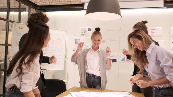 Coworker's team celebrates business success by fun dancing in a meeting.