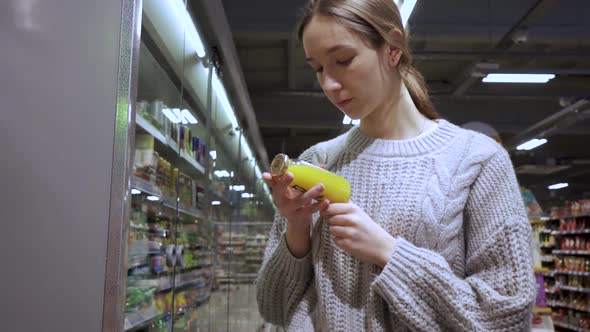 A Young Female Customer Reads the Composition of the Drink on the Juice Bottle