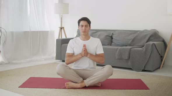 Relaxed Young Man in Sportswear Is Meditating in Lotus Position Sitting on Yoga Mat With Closed Eyes