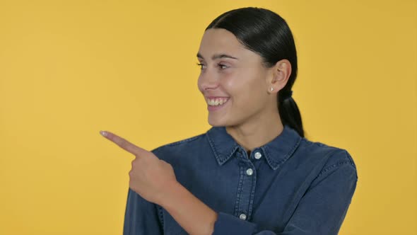 Latin Woman Pointing at Product Yellow Background
