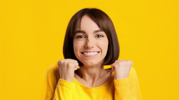 Joyful Brunette Female Shaking Fists Smiling Posing Over Yellow Background