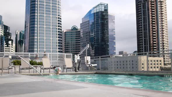 A young girl enjoys jumping in and out of a pool at a rooftop luxury hotel.