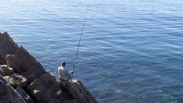 Man Enjoys Fishing with Rod Sitting on Adriatic Sea Rock