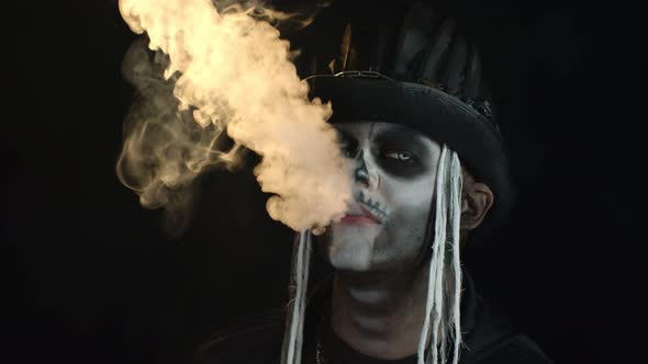 Sinister Man with Professional Skull Makeup Exhaling Cigarette Smoke From His Mouth and Nose