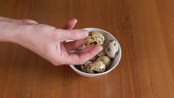 Female Hand Takes One Quail Egg From the Plate Examines It in Hand