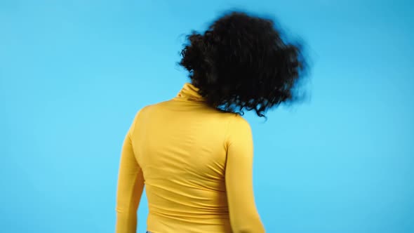 Unrecognizable Woman with Afro Hairstyle Dancing Positive Her Back on Blue Studio Background