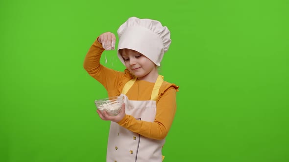 Child Girl Kid Dressed Cook Chef Baker in Apron and Hat Stir the Flour in a Plate Fooling Around