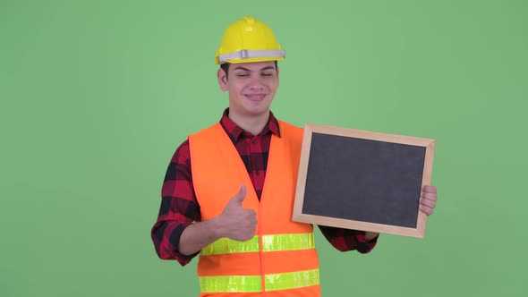 Happy Young Multi Ethnic Man Construction Worker Holding Blackboard and Giving Thumbs Up