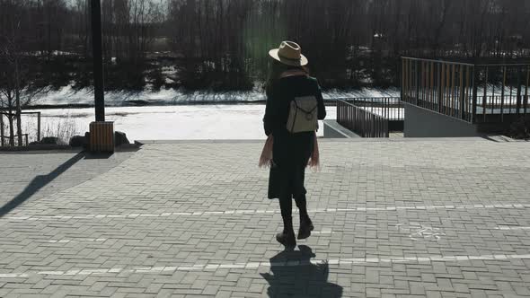 A Girl with Coffee Against the Backdrop of a Spring Park and a Snowy River