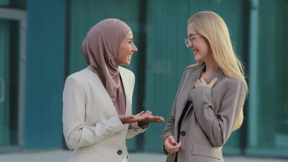 Young Blonde Caucasian Girl in Business Suit Talking to Friend Oriental Millennial Woman in Hijab