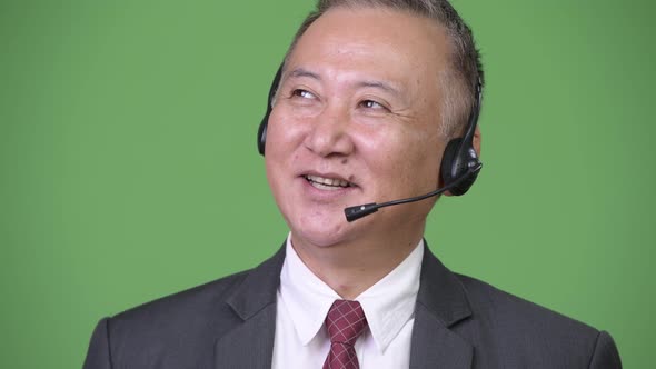 Mature Japanese Businessman Working As Call Center Representative Against Green Background