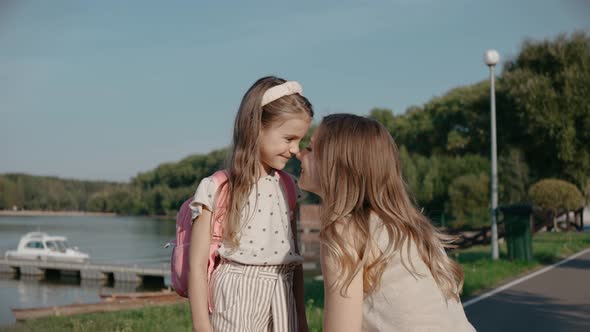 Woman Rubs Her Nose with a Smiling Daughter Near the Yacht Marina on a Sunny Day