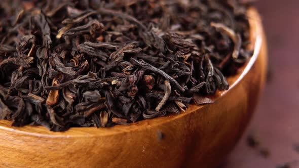 Dry black tea in brown wooden rustic bowl. Falling dried leaves in slow motion. Macro