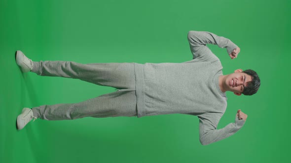 Full Body Of Smiling Asian Man Flex Muscle While Standing In Front Of Green Screen Background