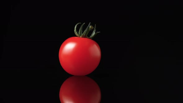 A Ripe Red Tomato with a Green Tail Rotates on a Black Reflective Kitchen Table Surface in Slow