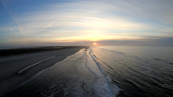 Aerial drone shot low over waves at a beach, on a calm evening