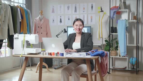 Asian Female Designer In Business Suit Working On A Laptop And Smiling To The Camera While Designing