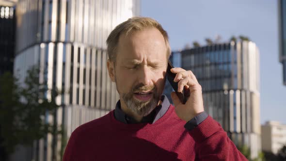 A Middleaged Handsome Caucasian Man Talks on a Smartphone in a Street in an Urban Area