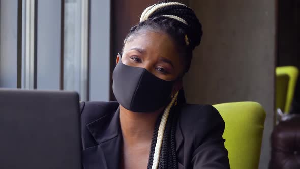 African American Woman in Cafe Works on Her Laptop. Black Girl in a Protective Mask with a Laptop