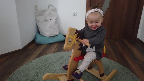 Happy baby girl playing on wooden rocking horse. Childhood, game at home concept