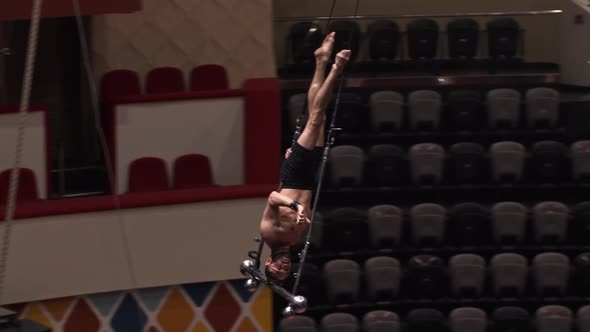 An Acrobatic Man Doing a Show on the Flying Construction on Circus Arena  Standing Upside Down