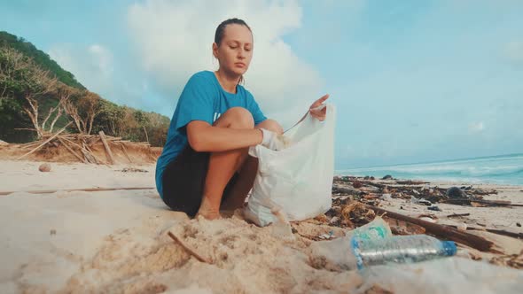 Young Caucasian Woman Volunteer Sits on Ocean and Cleaning Beach From Rubbish