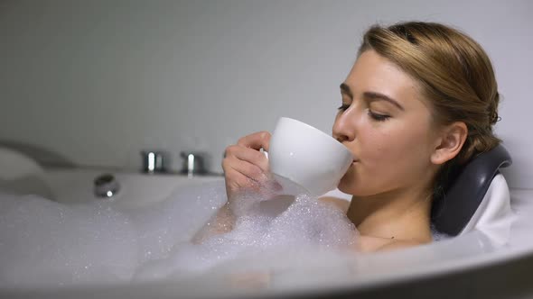 Smiling Woman Enjoying Coffee in Bath With Foam Bubbles, Evening Relaxation