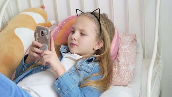 a Pretty Little Girl in a Rim with Cat Ears with a Phone in Bed