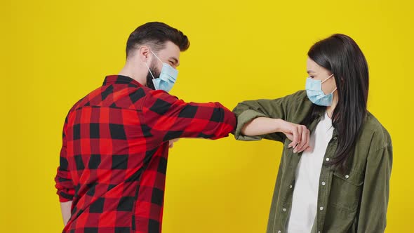 Portrait of a Man and Woman in Medical Protective Masks Greeting Each Other with Their Elbows on an