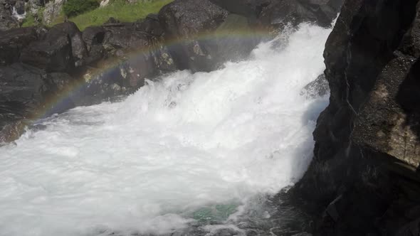 Water Cascading Over Rocks With Mist Creating Rainbow Above