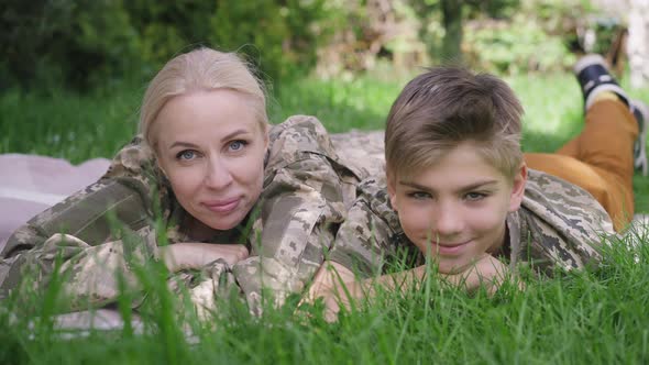 Front View Portrait of Happy Caucasian Military Woman and Teenage Boy Lying on Green Lawn Looking at