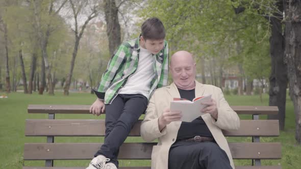 Portrait Cute Grandfather and Adorable Grandson Sitting in the Park on the Bench