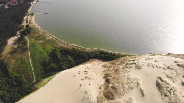 AERIAL: Flying backwards and revealing the dead sand dunes near the Baltic Sea and the green pine fo