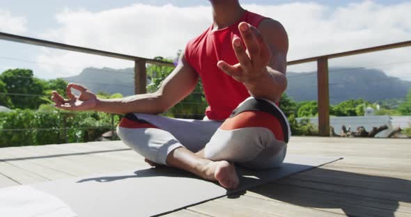 Midsection of relaxed biracial man sitting on terrace and meditating