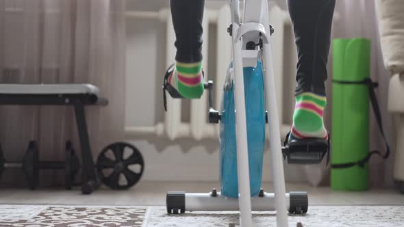 Legs Pedaling an Exercise Bike at Home in a Room Closeup View