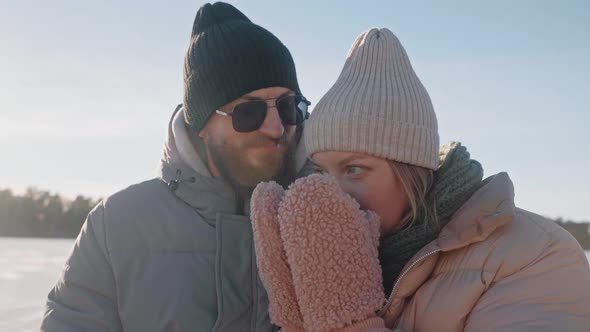 Cute Couple Drink Hot Tea From Thermos and Kiss Sitting on a Dock in Winter