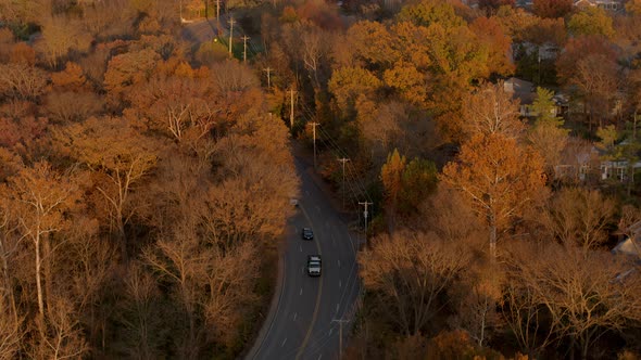 Aerial over a winding road near a church in autumn as cars drive past camera tilts down