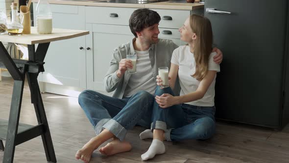 Young Couple Sits on the Floor of Their Kitchen and Drinks Delicious Milk