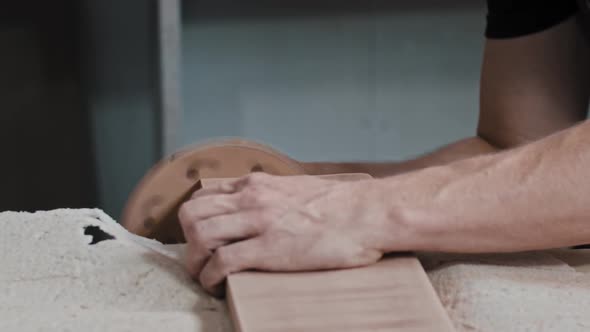 Man Worker Makes the Side of a Rectangular Wooden Detail Softer Using a Grinding Machine