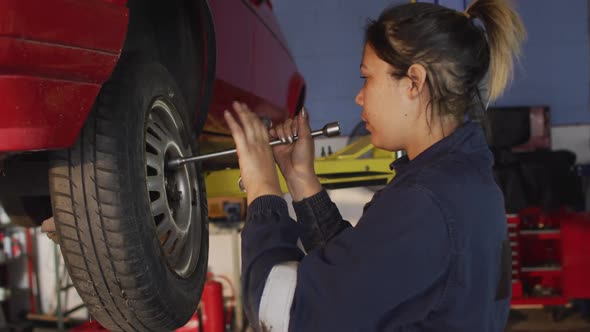 Female mechanic changing tires of the car using a wheel wrench at a car service station