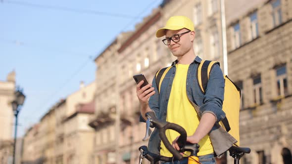 Portrait of a Happy Delivery Man Who is Standing and Holding a Smartphone