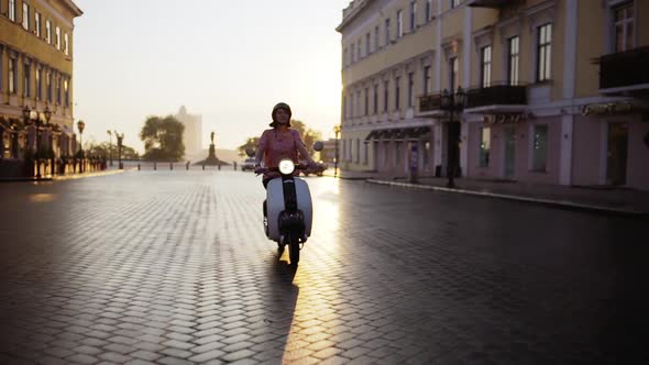 Young Beautiful Girl Riding Around City on Scooter at Sunrise