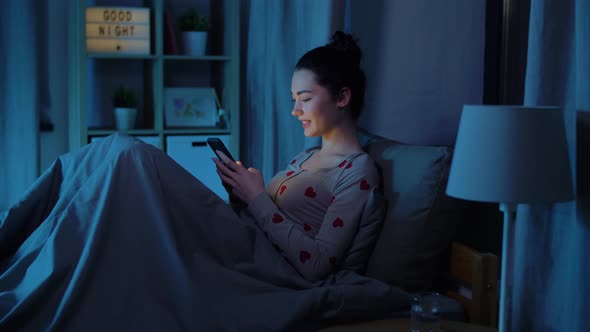 Teenage Girl in Pajamas with Phone in Bed at Night