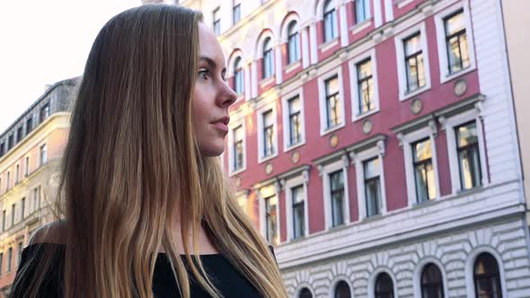 Young Beautiful Woman Looks Around in the City - Buildings in the Background