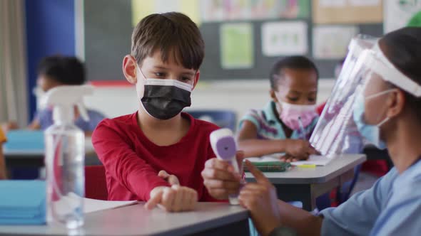 Diverse medical worker showing schoolboy how to measure temperature, all wearing face masks,