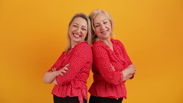 Medium Studio Shot on Yellow or Orange Background of Two Adult Caucasian Female Friends Standing