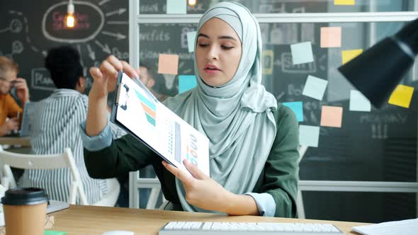 Portrait of Muslim Businesswoman Making Video Call From Office Speaking Showing Charts