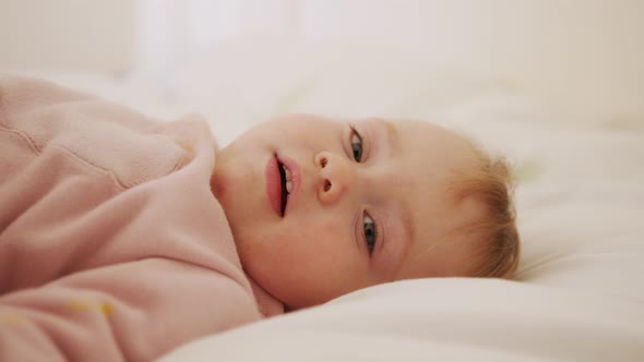 Cute baby girl sitting on a bed, playing, rolling and laughing