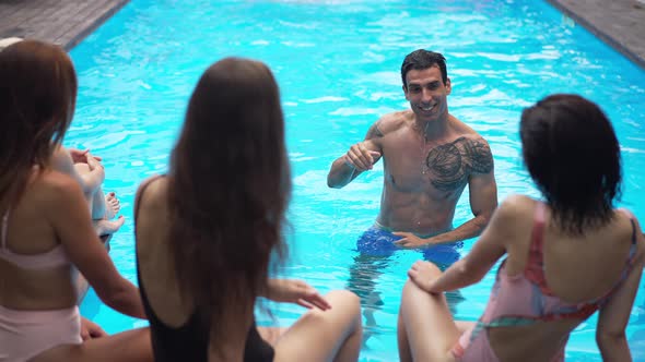 Positive Wet Middle Eastern Handsome Man Standing in Blue Swimming Pool Talking with Caucasian Women