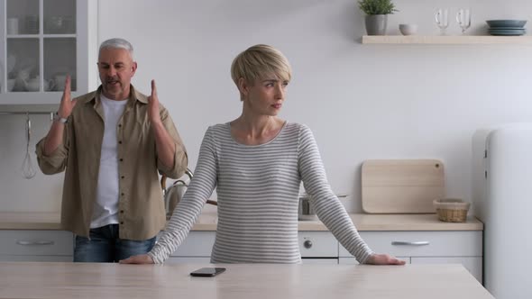 Unhappy MiddleAged Couple Having Quarrel Standing In Kitchen At Home